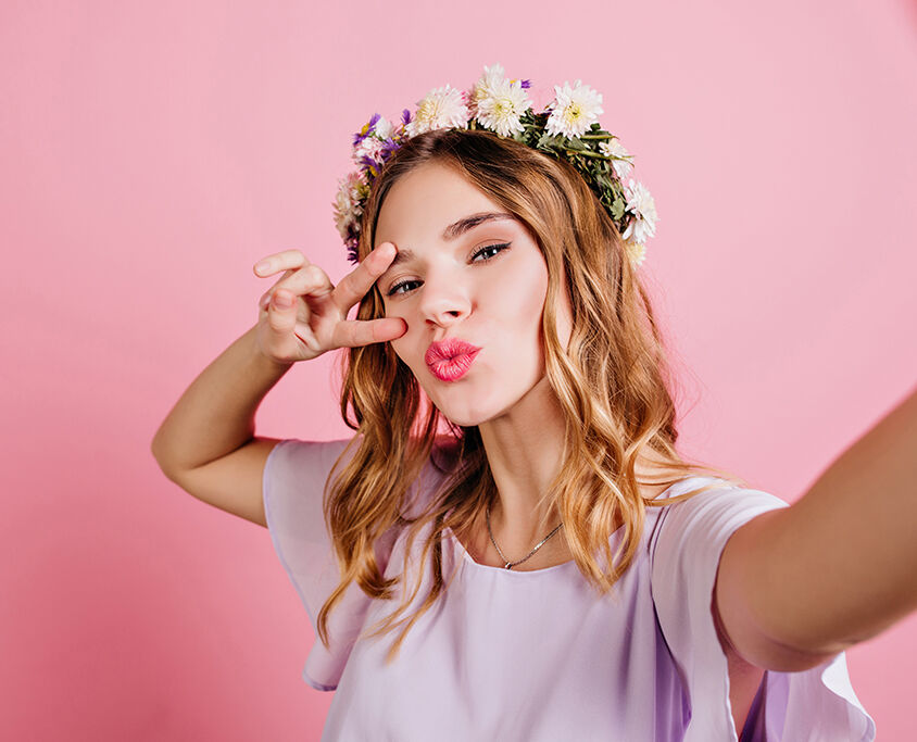 Close-up portrait of enchanting white girl wears trendy flower wreath. Charming european lady with blonde hair making selfie on pink background..